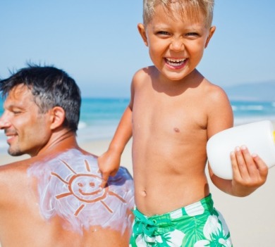 little boy putting sunscreen on his dad on the beach | SeaShore Realty